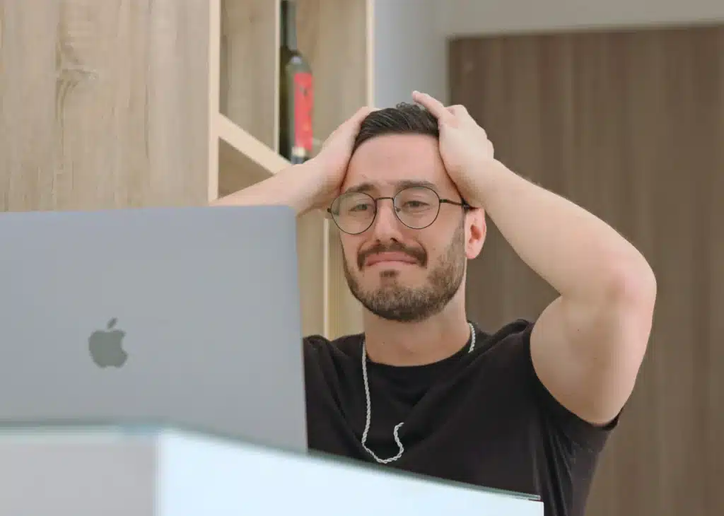 Photo of a man grabbing his head while looking disappointedly at his MacBook screen