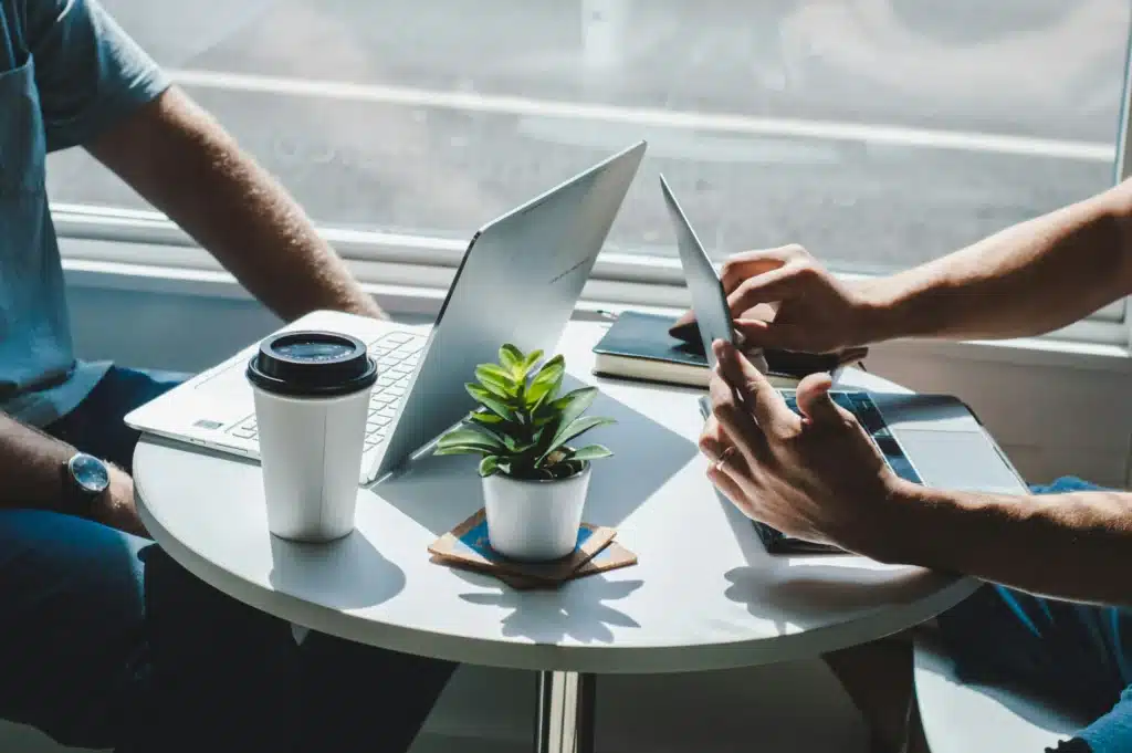 Photo of two men sitting at a small round table working on laptops