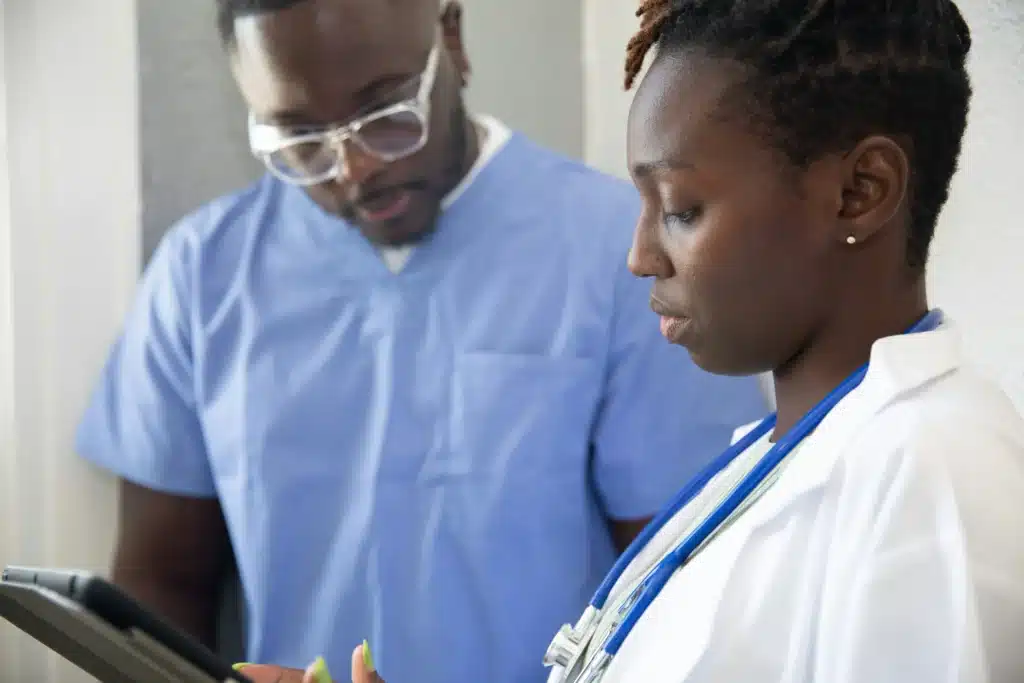A male and female doctor wearing scrubs and a lab coat looking together at an iPad