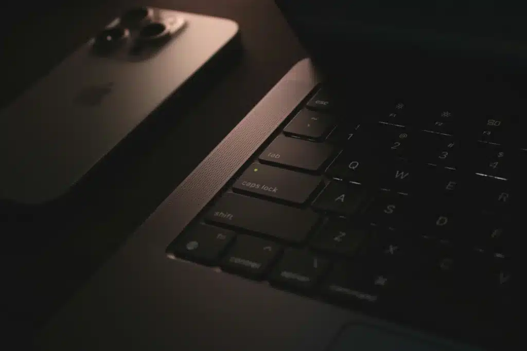 Dark photo of Mac keyboard with caps lock on next to iPhone