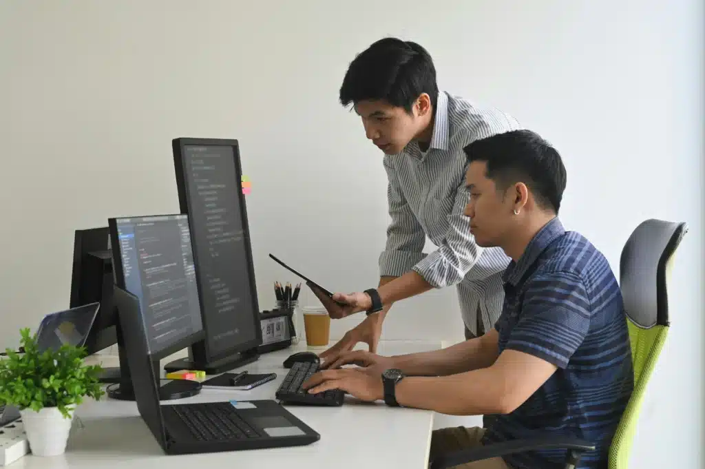 IT support Newmarket - two asian men working at a desktop computer together.