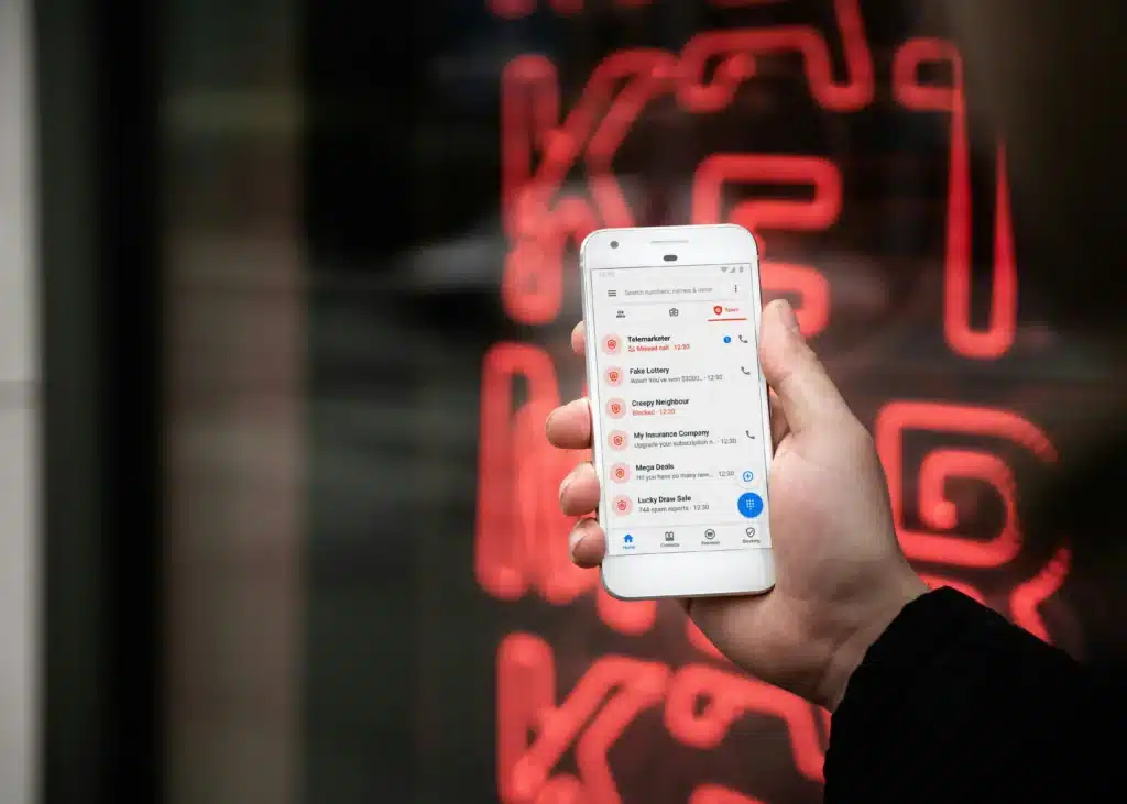 Hand holding up iPhone with fraudulent emails open on the screen