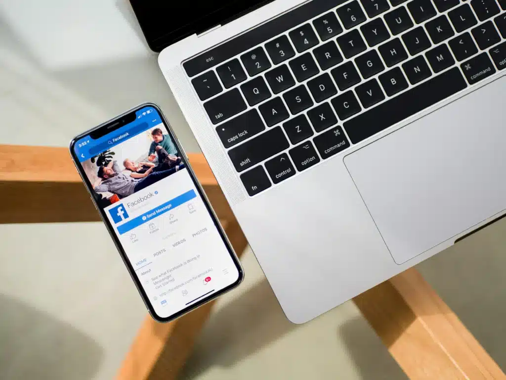 iPhone on a glass table next to a macbook with facebook open