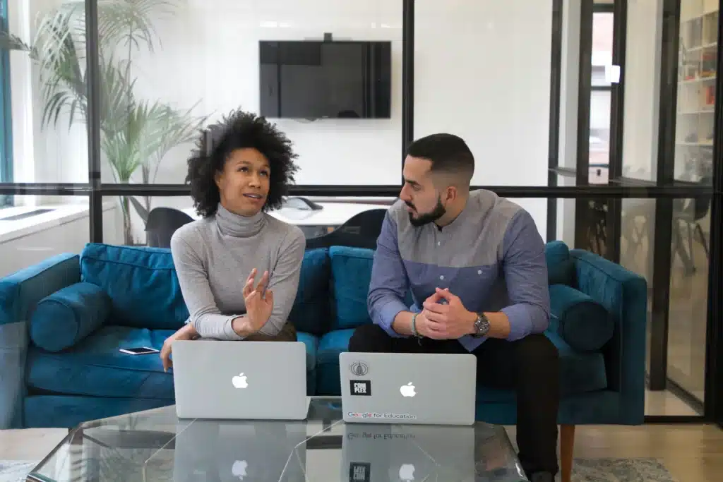 Mac IT services in office with man and woman talking on blue sofa in front of Macbooks