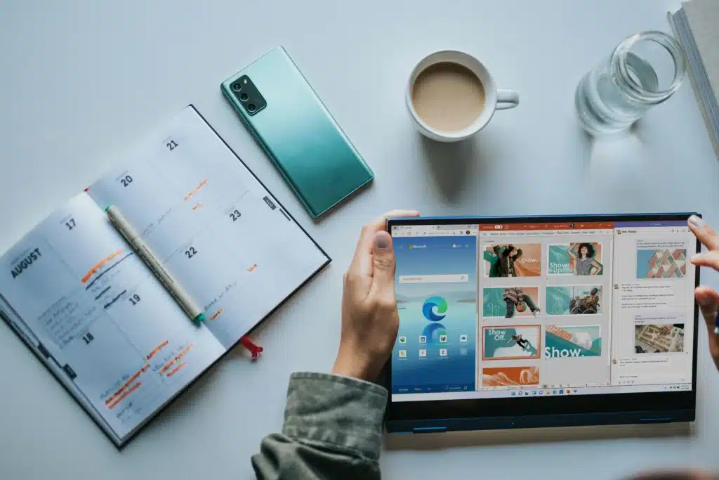 Man holding Microsoft Surface with apps open above desk with drinks, notebook, and phone