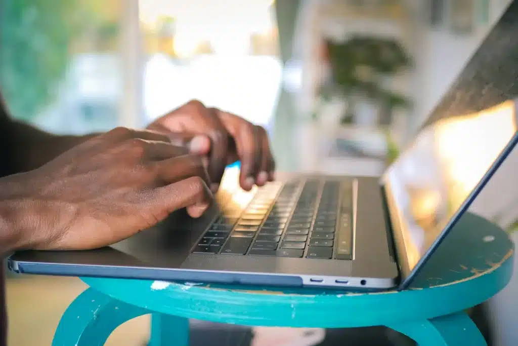 Man's hands typing on Macbook Pro on top of aqua wood table