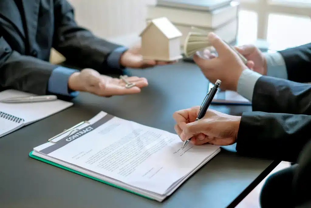 Men sitting at meeting table exchanging cash for a key and signing a contract