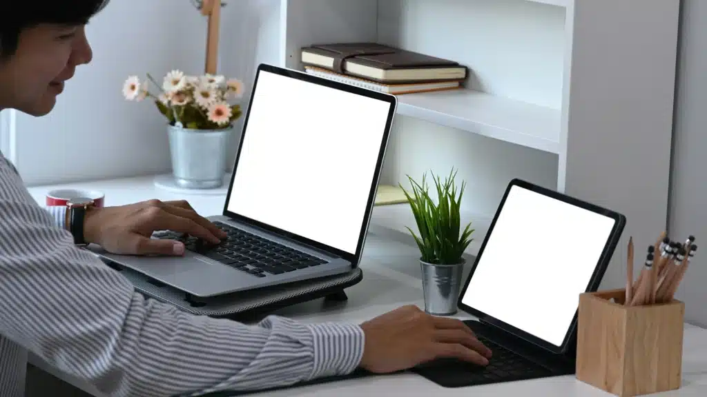 Photo of a man sitting at a desk working on a MacBook and a tablet with blank screens