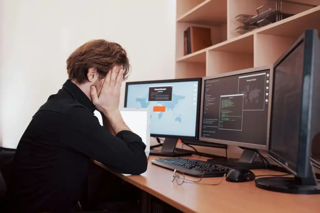 Photo of a man sitting in front of two desktop screens with his face in his hands