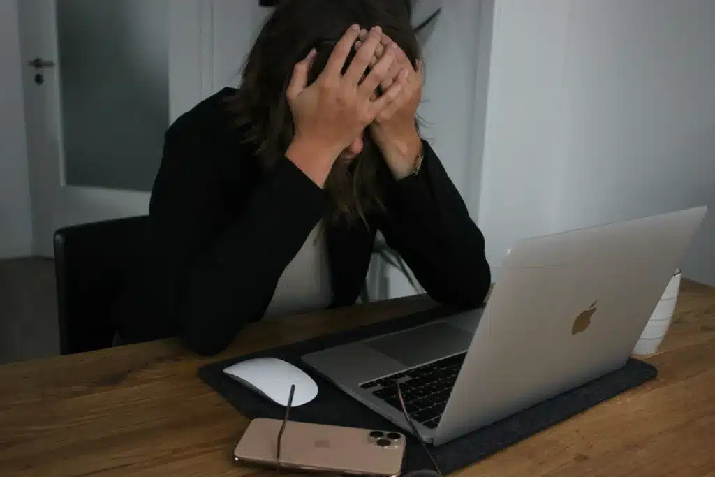 Photo of a woman holding her head in her hands as she works at a table on a MacBook
