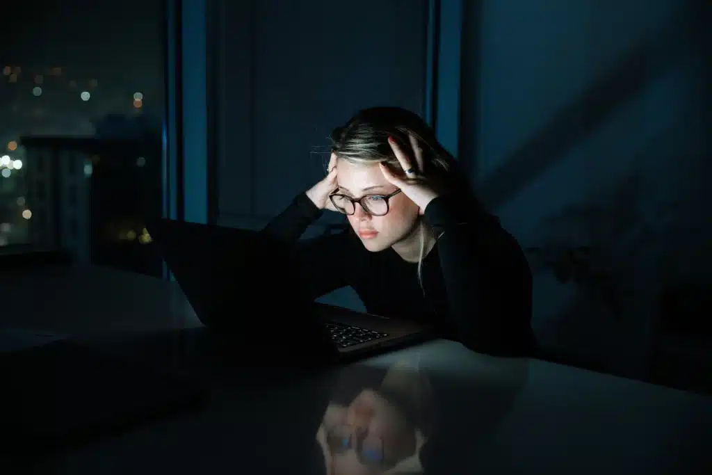 Photo of a woman staring at a laptop screen with a frustrated expression at nighttime