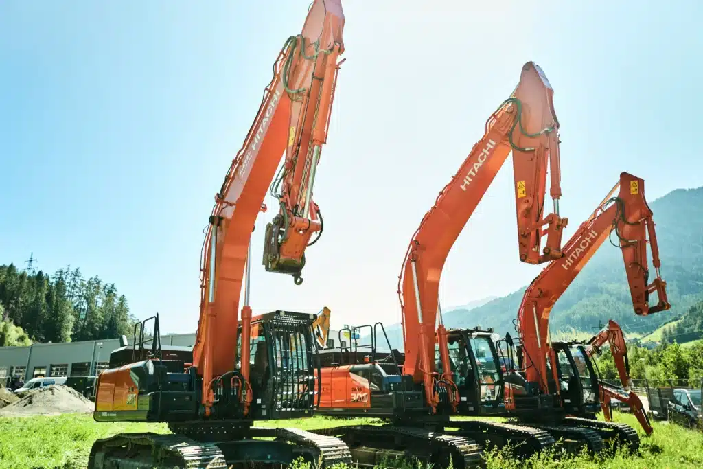 Three orange construction cranes lined up in grass field