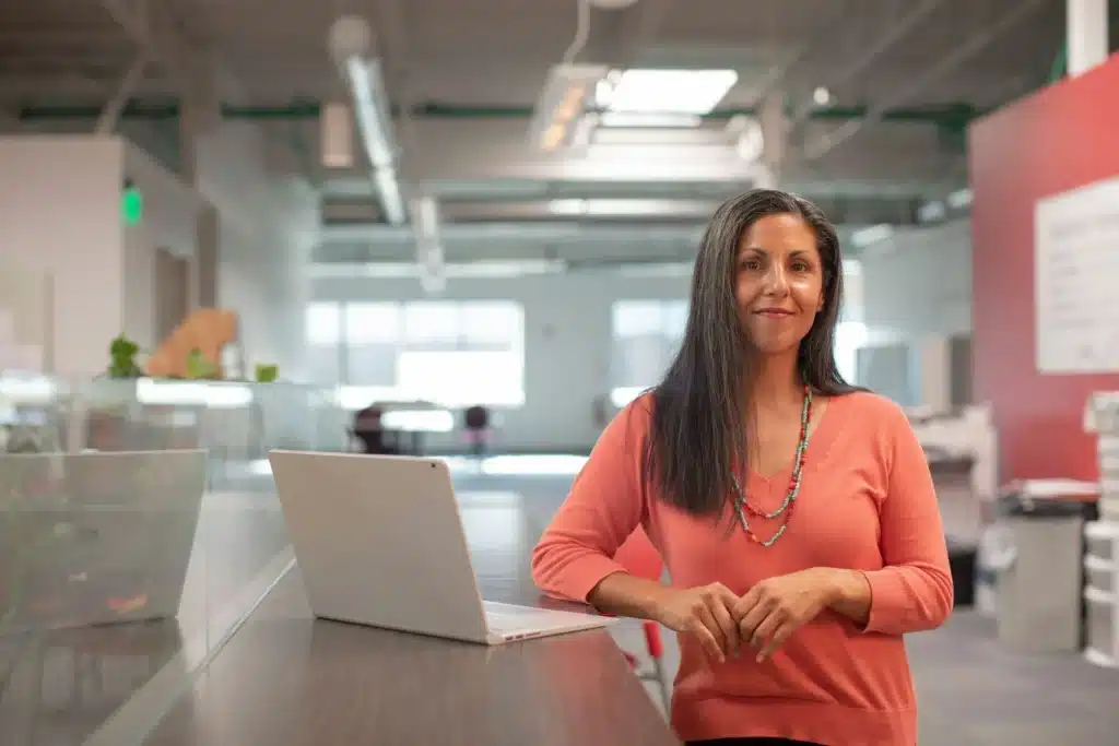 Woman in office smiling at the camera next to laptop