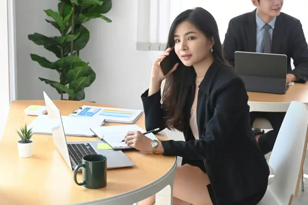 Woman sitting in office at round table holding pencil and iPhone