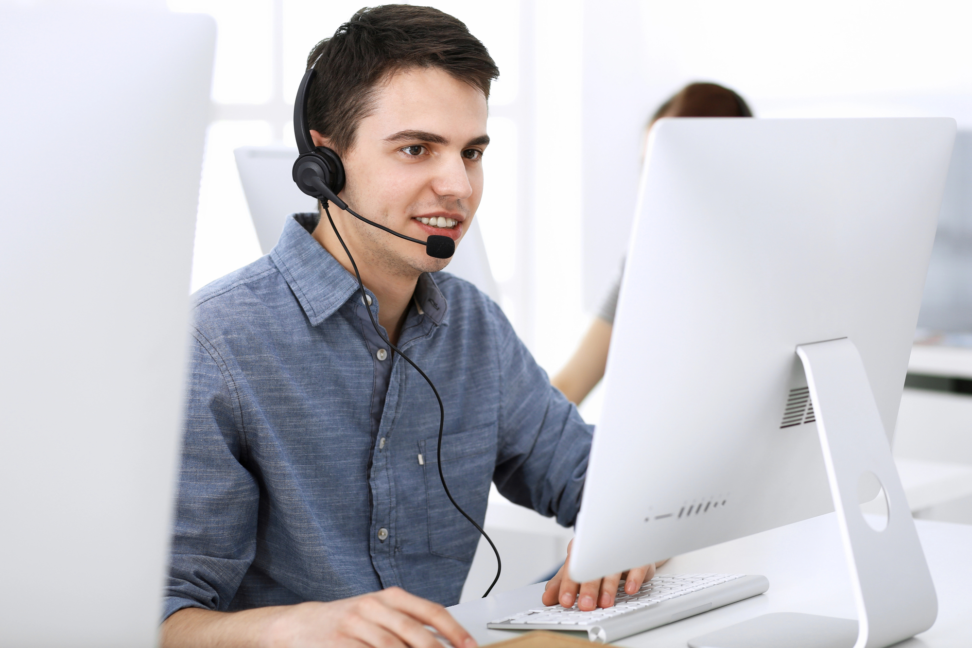 IT support specialist assisting a client through a headset while working at a desktop computer in a modern office environment.