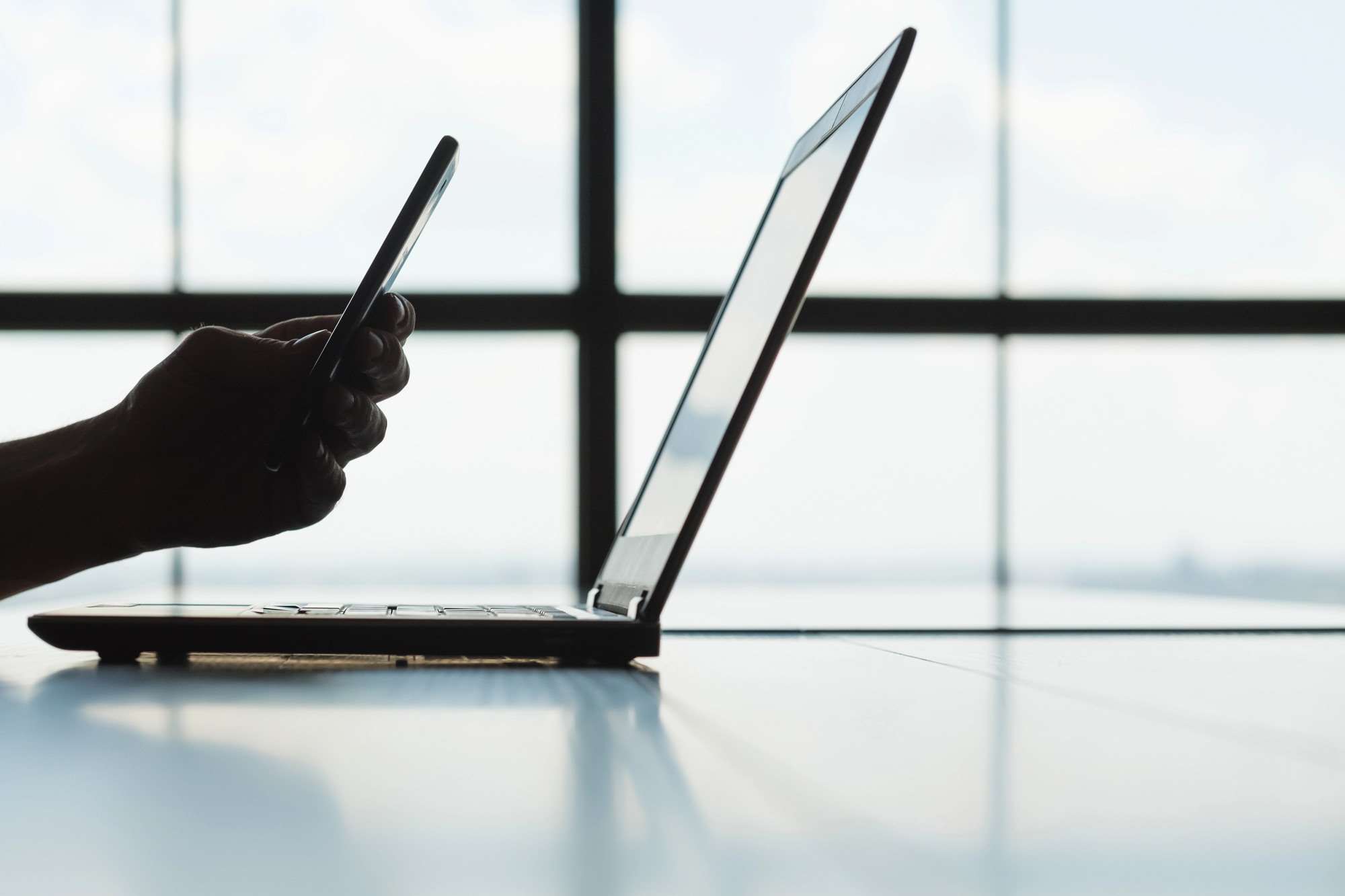 Person using a smartphone beside a laptop, representing the shift from SMS authentication to more secure authenticator apps for improved account security